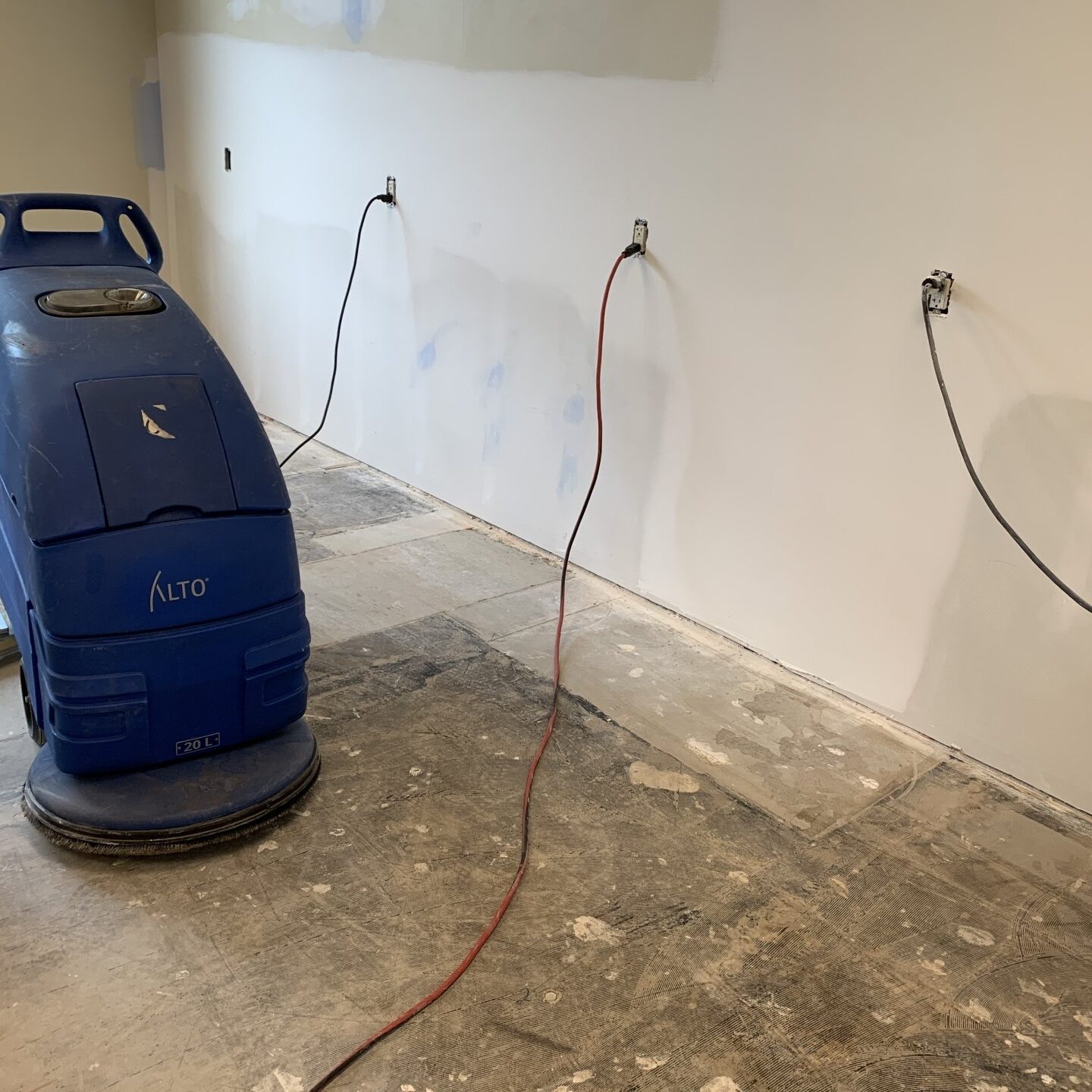 Floor cleaning machine plugged into a wall outlet on a construction site with unfinished flooring.